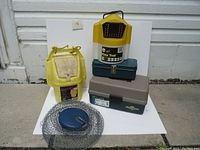 Photo showing full lot including all fishing boxes, reels, bait bucket, live well aerator, and wire basket trap arranged in front of a white door on a white surface.