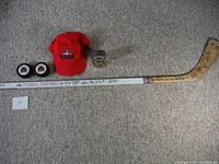 Full view showing the signed hockey stick laid on carpet next to the red Florida Panthers hat and two black hockey pucks with logo, also tape dispenser is visible