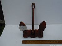 Front view of the heavy boat anchor showing the shank with eyelet and two flukes, placed next to a 12-inch ruler for scale.