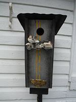 Front view of the birdhouse showing the portion where the bird enters, the attached white Harley Davidson motorcycle model, and the Harley Davidson logo plaque at the bottom.