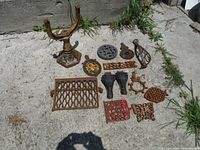 Overview of various cast iron pieces laid out on concrete ground showing diverse shapes and sizes including lattice panels, furniture legs, and gears.