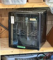 Front view of compact black Avingarde wine fridge showing glass door and metal wire shelves inside.