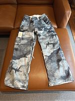 Full view of the snowboard pants showing the black and grey tie-dye pattern and cargo pockets.