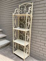 Front view of the folding wrought iron shelving unit showing the full height, four shelves, and floral scrollwork on the sides and back.