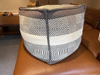 Cube-shaped ottoman on brown leather couch, detail of side showing grey and white geometric woven pattern.