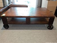 Front view showing low-profile pine plank top, metal side panels, two open cubbies and four spoked wheels