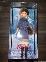 Front view of Russia Barbie doll in original sealed box showing full doll with fur hat, blue coat, beige skirt, and fur muff.