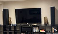 Front view of Samsung 75" TV on black shelving with speakers and décor