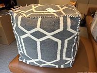 Poof ottoman showing grey and white geometric fabric and stitched edges on a brown leather chair.