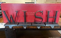 Photo of the full set of WISH metal stocking hangers on a table with the original Pottery Barn box in the background, showing the letters and their design.
