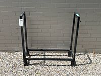 Black wrought iron log holder rectangular frame seen from one side, showing open base and vertical sides.