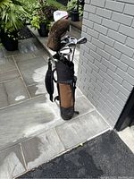 Full view of complete golf club set in stand bag showing clubs and bag from side angle on tiled floor near gray brick wall.
