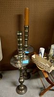 Pair of tall brass candle holders with candle, one holding an orange candle.