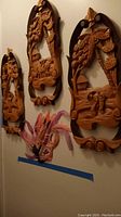 Set of three wood carved wall art panels hanging on a wall with a decorative feather mask below them.