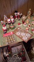 Small decorated Christmas ornaments including Santa, snowman, nutcracker, angel figures, and gold bells on green textured surface
