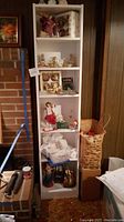 Full view of white vertical bookcase holding assorted Christmas items including angels and ornaments.