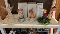 Shelf with clear glass angel, two ceramic music box angels, teddy bear figurine, and wooden horse on white shelf