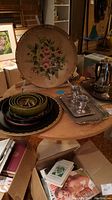 Wide view of round wooden pedestal table with multiple trays and accessories on top and cardboard box below