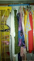 Photo of hanging women's clothing on rod with yellow hanging shoe/accessory organizer and visible belts