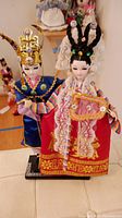 Pair of tall Oriental dolls posed standing on a black base, showing front full view of both dolls in traditional outfits