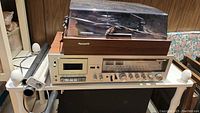 Panasonic turntable with clear dust cover on top of white shelving unit.