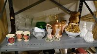 Metal shelving unit shelf with various glassware, ceramic cups and teapots including floral patterned cups and pink ceramic teapot.