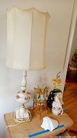 Full view of the tall floral ceramic lamp with off-white fabric shade, oriental folding lantern lamp with gold accents, and seashell shaped lamp on table.
