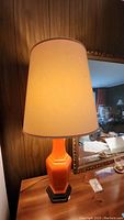Single red ceramic lamp with beige shade on a wooden table against paneled wall