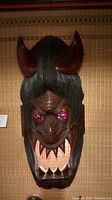 Close-up of grotesque mask face with red horns and lighted eyes lit pink and green.