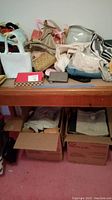 Table top with assorted purses including leather, beaded, cloth, and crocheted types, along with caps and scarves, with two storage boxes containing more items visible underneath.