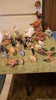 Overall view of assortment of small animal figurines on green cloth background including wooden, ceramic and resin pieces