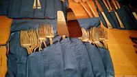 Blue roll displaying twelve dinner forks and twelve salad forks alongside a cake server and knives