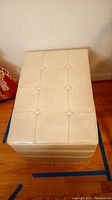 Top view of closed beige storage ottoman showing tufted design with buttons