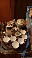 Black and gray Japanese teapot, six small matching tea cups, green and gold teapot on a lacquered tray with floral design.