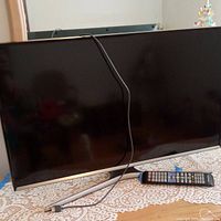 Front view of Samsung flat screen TV on table, showing screen, connected HDMI cable, and remote control.