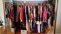 Wide view of assorted women's clothing on hangers including dresses, tops, and jackets across a mirrored closet rod.