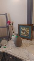 Lot items arranged on marble countertop next to sink, including vases and framed print.