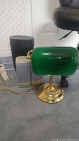 View of desktop lamp with green glass shade, brass base, and adjustable tilt, shown with Umbra trash bin, GPM speakers, and power bar.