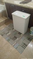 Photo of white woven hamper on bathroom floor with patterned mat underneath