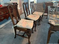 Full row of four wooden dining chairs with floral removable cushions on woven rush seats. Dark wood with carved legs and backs.