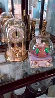 View of the anniversary clock, music snow globe, and two candle holders arranged on a glass shelf.