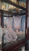 Photo showing crystal and glass items including large textured glass vases, a glass bowl, and the glass boat sculpture in the foreground within a display cabinet.