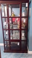 Front view of the wood framed curio cabinet with beveled glass and five glass shelves inside, mirrored back visible, lights mounted at top inside.