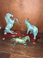 Front view of two larger figurines (horse and elephant) on wooden bases and smaller horse figurine on floor.