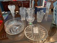 View of all seven glass and crystal items arranged on wooden table, showing the variety including four vases, two bowls, and one platter