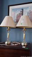 Two matching table lamps standing side by side on a wooden surface with picture frame in the background.