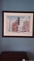 Framed print hanging on blue wall, showing winter cityscape with flatiron building and modern buildings