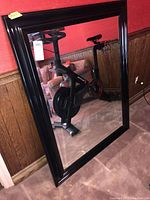 Full view of mirror leaning against wall showing entire piece and dark glossy frame with beveled glass