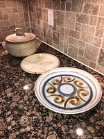 Photo showing the lidded serving bowl with a handle on the lid, alongside a smaller plate and a larger decorative platter with swirl design.