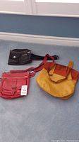 Photo showing three purses: one small black Roots crossbody purse with multiple pockets, one red Roots bag with tags, and one two-tone brown and mustard yellow Anthropology tote bag